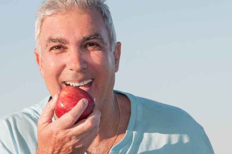 Smiling man biting an apple with restored teeth